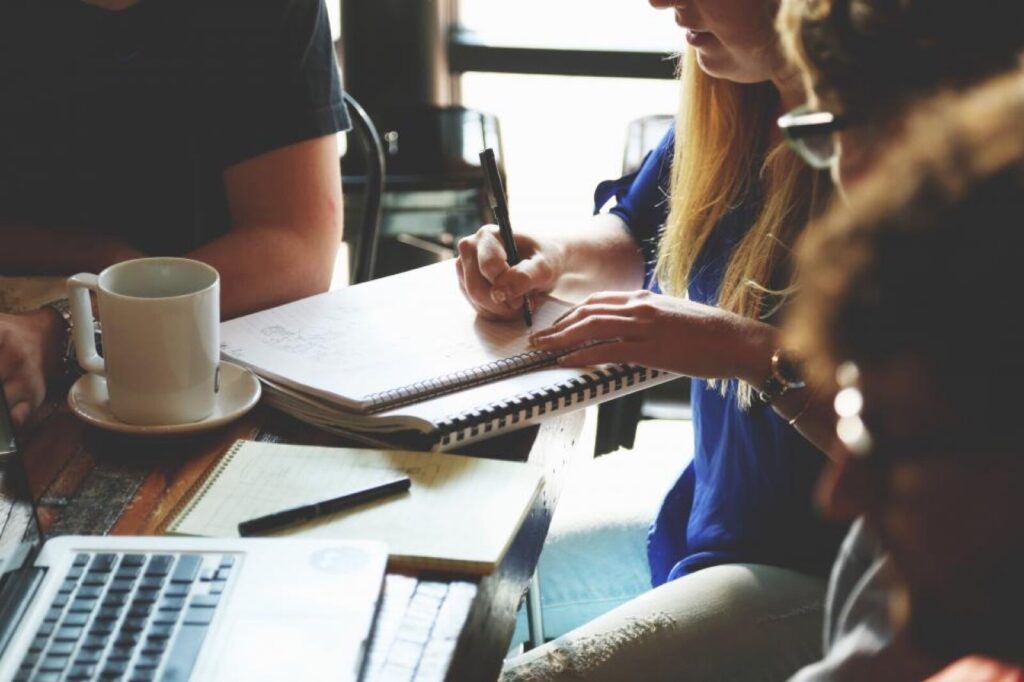 A small team working together around a table with a notebook and laptop