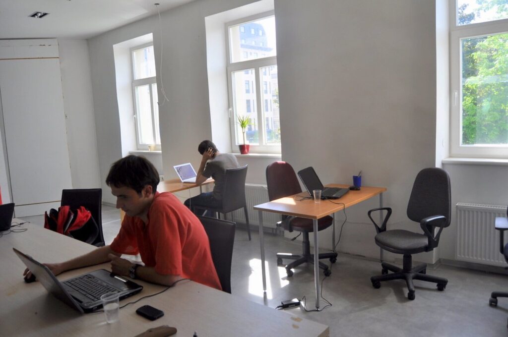 Two people working on laptops at desks in a bright shared startup office