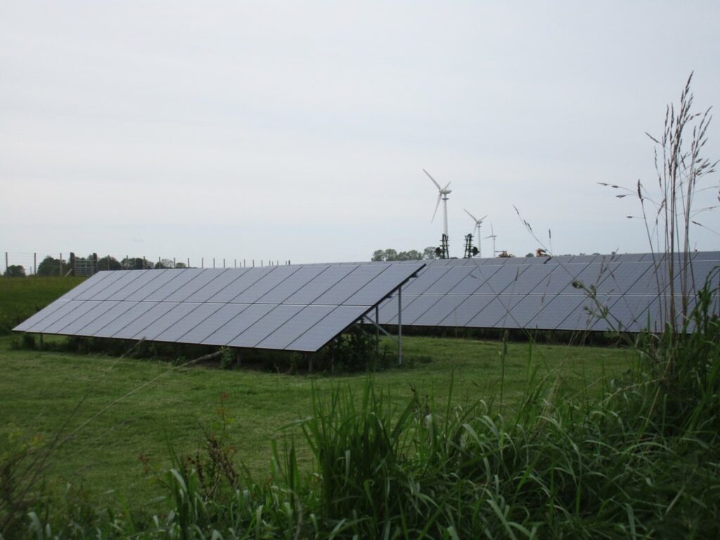 A solar array with wind turbines behind it in a UK field